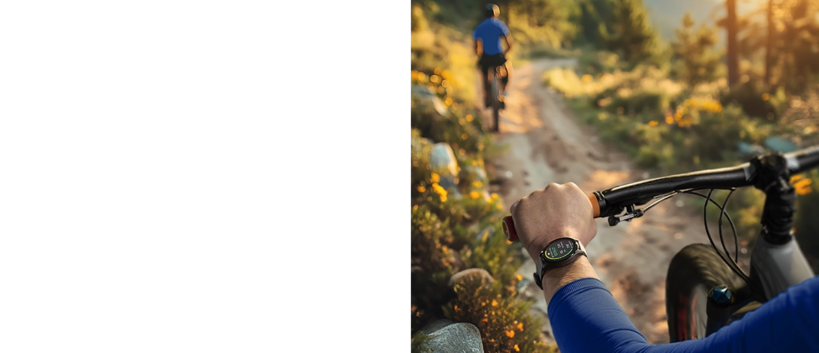 Over-the-shoulder view of a cyclist riding along a gravel road surrounded by green meadows, wearing a Hama smartwatch on his left wrist.