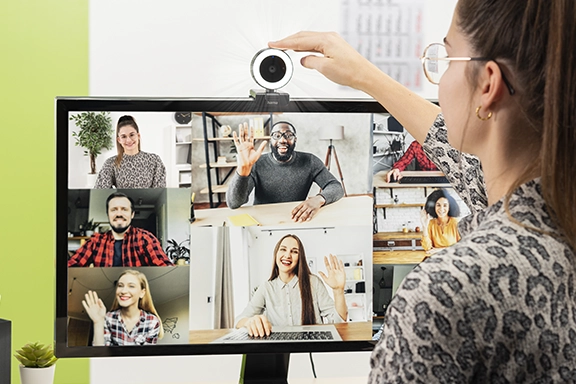 A young lady is sitting at her desk and has a video call. She activates the ring light of the "C-850 Pro" webcam at the touch of a button.