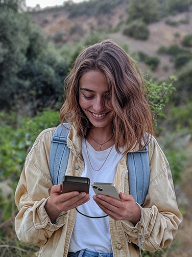 A young woman is hiking in nature and uses her smartphone while charging it with the Hama Power Pack "PD 20"